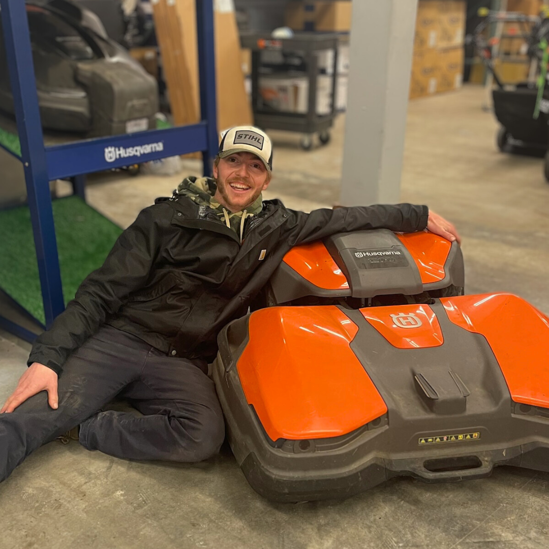 Dylan smiling and sitting next to a Husqvarna Ceora Automower