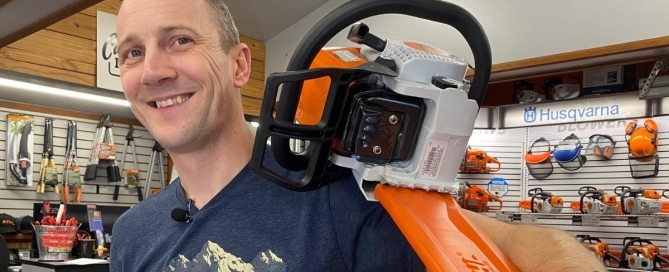 man smiling, holding chainsaw as it sits on his shoulder