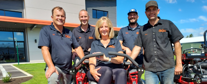 Carl's Mower & Saw family gathered around a Gravely mower in front of their new building