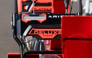 Closeup image of an Ariens Deulxe Snow Thrower in a lineup of similar snow blowers sitting outside