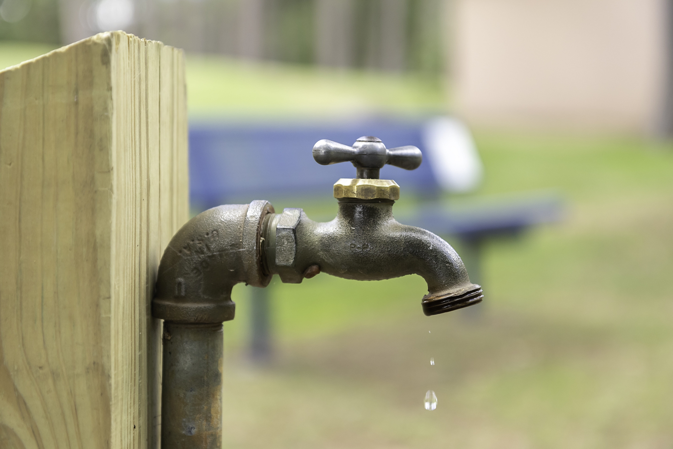 Image of an outdoor water spigot with a slow leak as a drop of water comes out